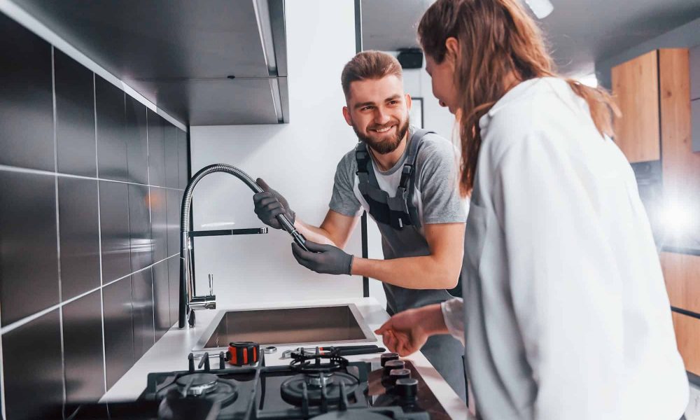 young-professional-plumber-in-grey-uniform-shows-results-of-work-for-housewife-on-the-kitchen.jpg