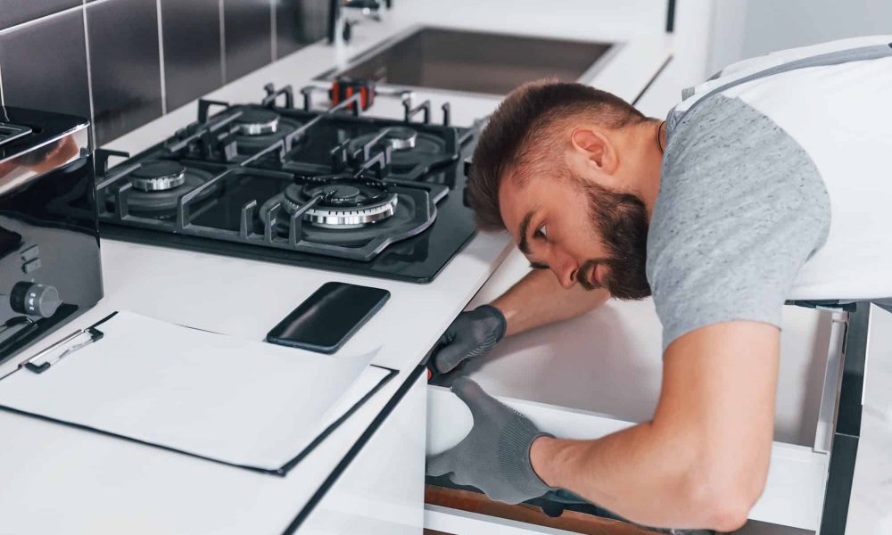 young-professional-plumber-in-grey-uniform-working-on-the-kitchen-2.jpg